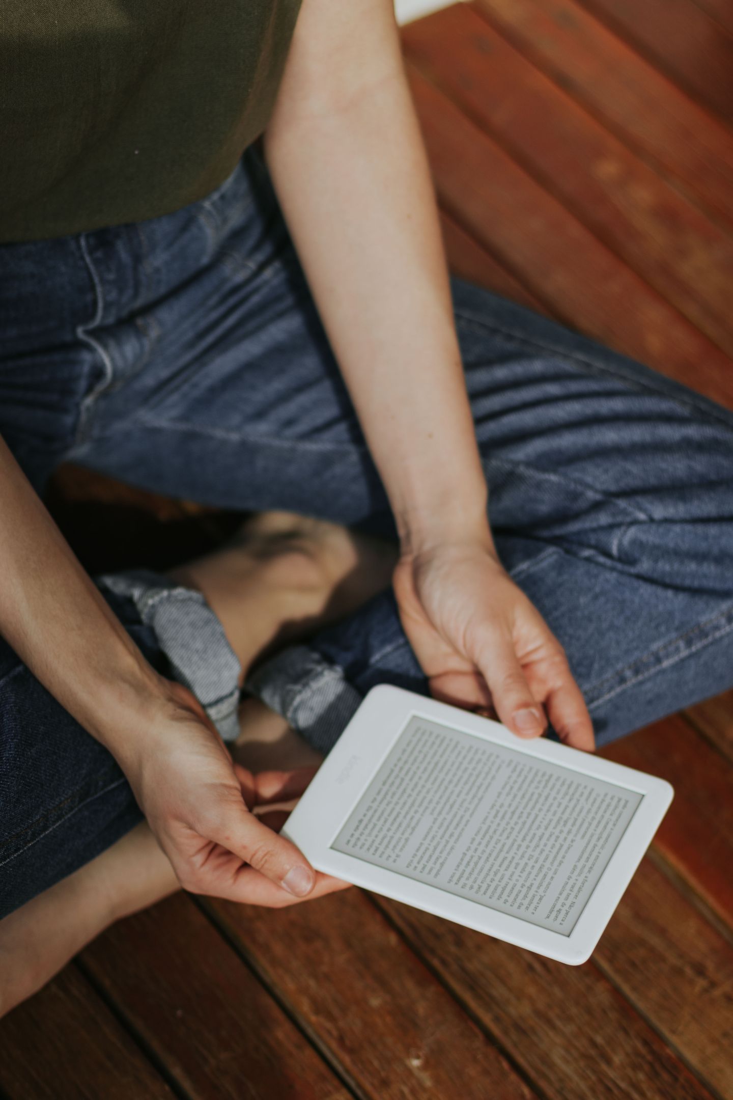 Person holding an ebook reader while sitting on a wooden deck
