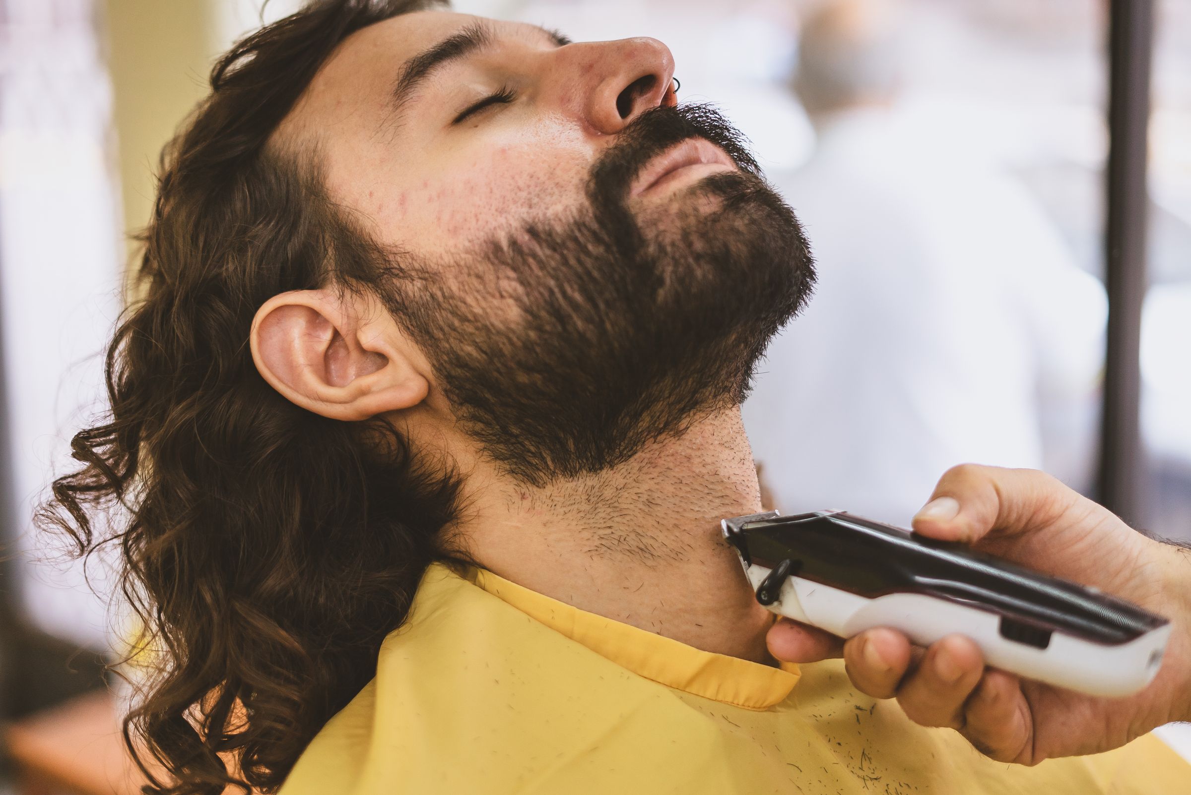 Barber using an electric shaver carefully along a customer's beard