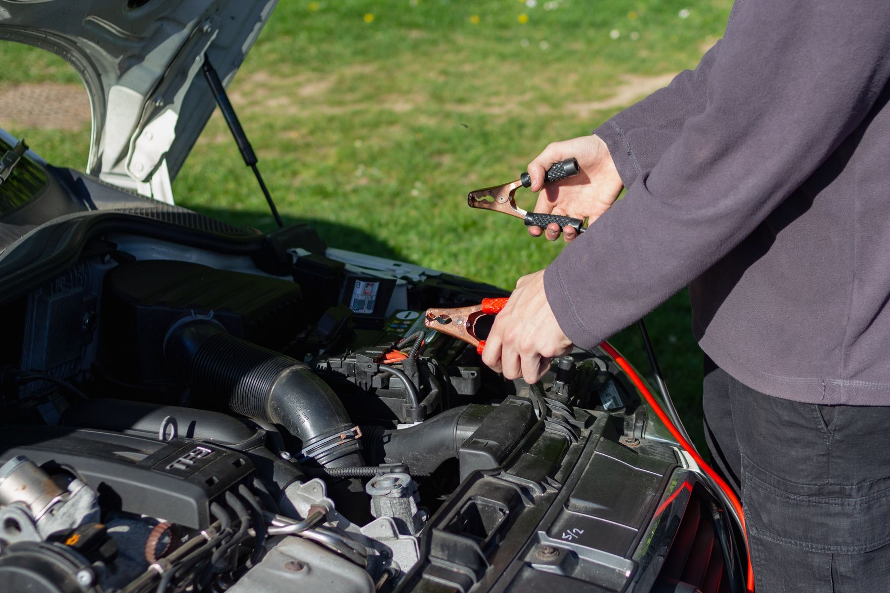 Person connecting charging clamps under a car bonnet
