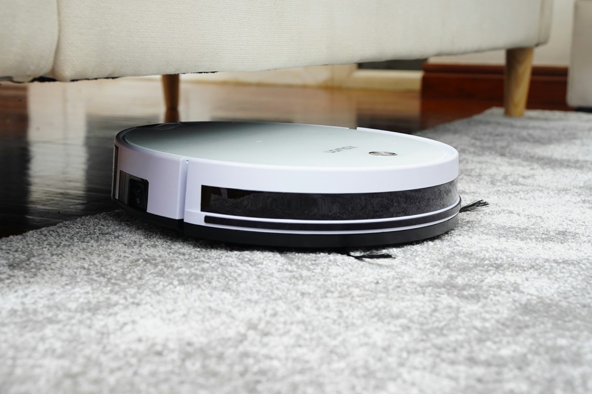 Robot vacuum moving across a hard floor beside a rug