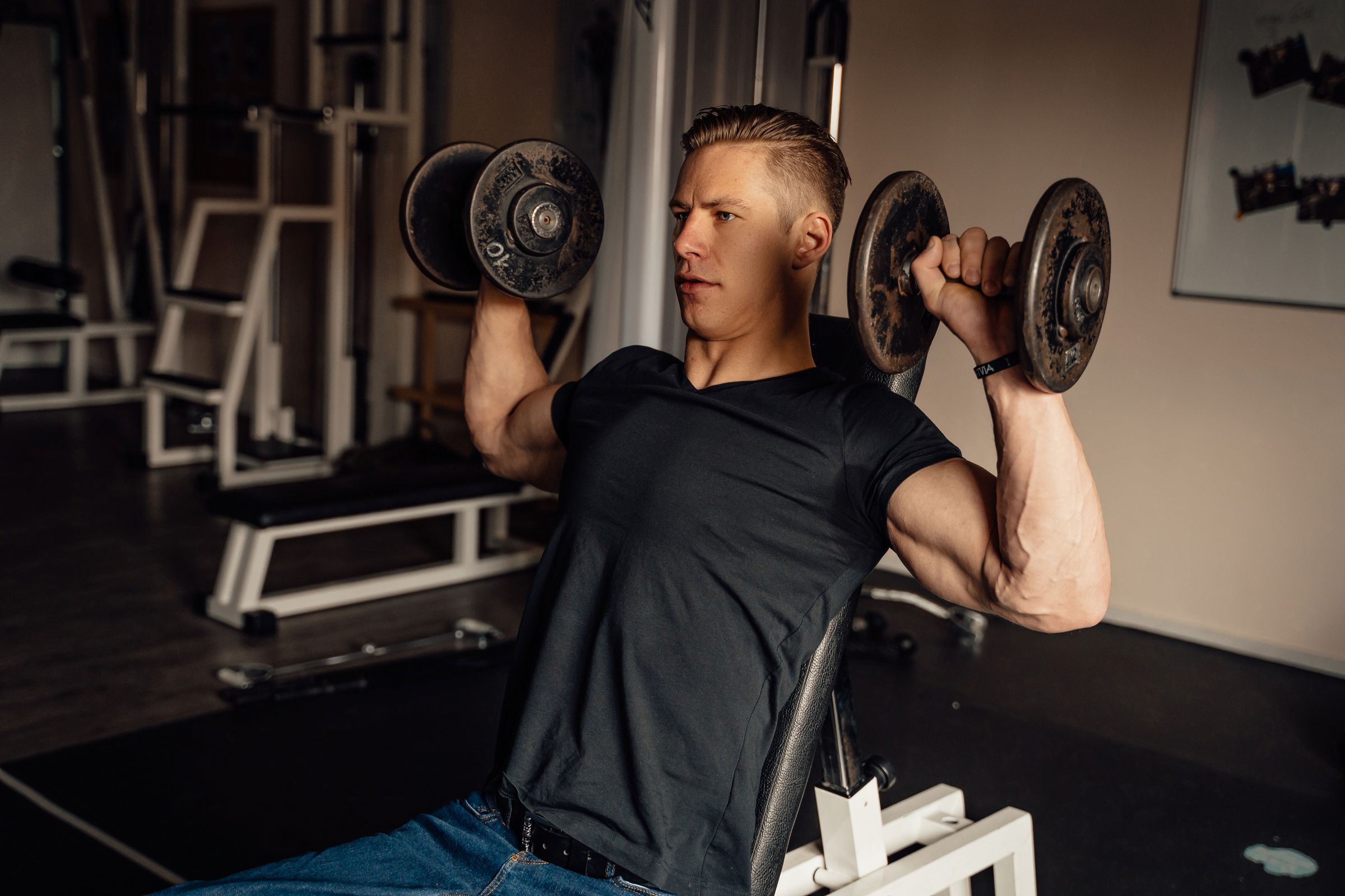 Man performing a controlled dumbbell shoulder press in a gym