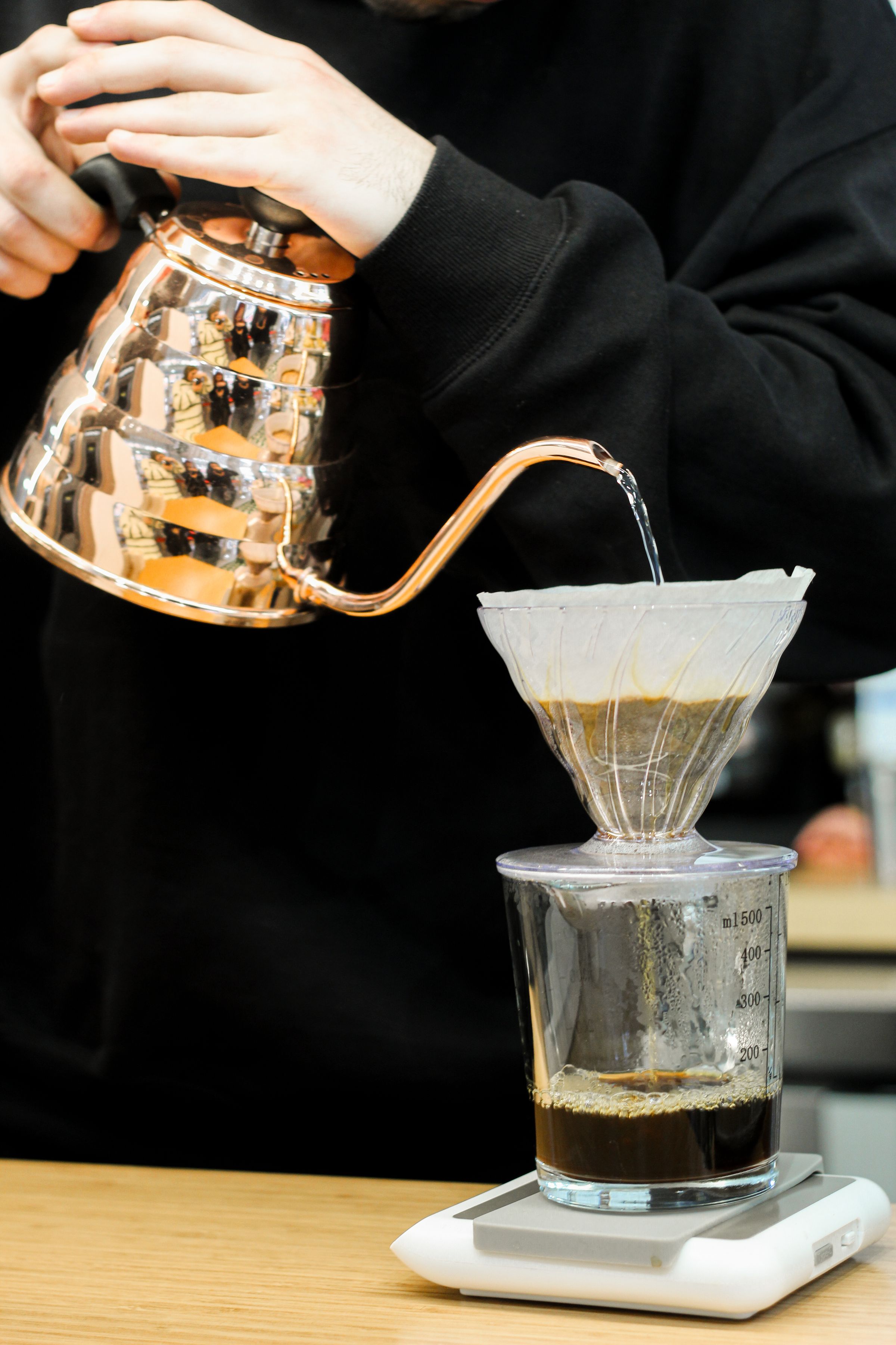Hands pouring water from a copper gooseneck kettle over coffee